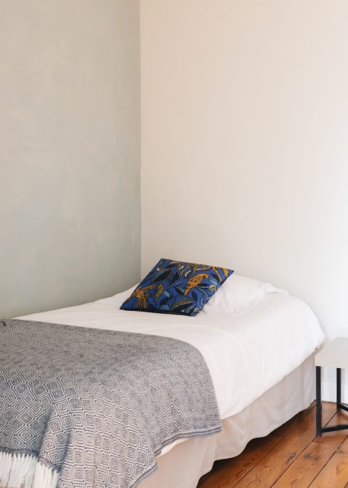 Chambre minimaliste à La Maison D'olivier avec lit blanc, coussin bleu décoratif, parquet et murs neutres à Mesnard
