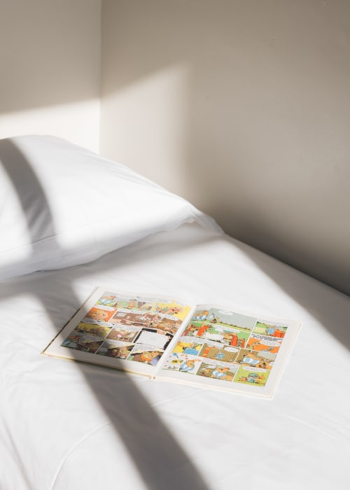Bande dessinée ouverte sur un lit blanc avec oreillers à La Maison D'olivier B&B à Mesnard La Barotière
