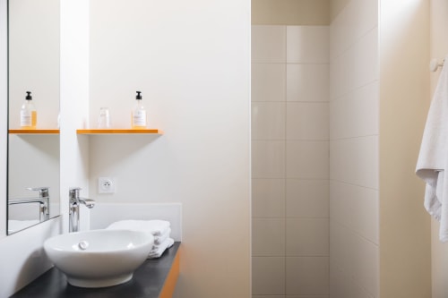 Salle de bain moderne à La Maison D'olivier avec vasque blanche, étagères oranges et zone de douche carrelée