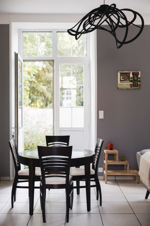 Salle à manger du cottage La Maison D'olivier avec table noire, chaises et luminaire suspendu moderne donnant sur le jardin