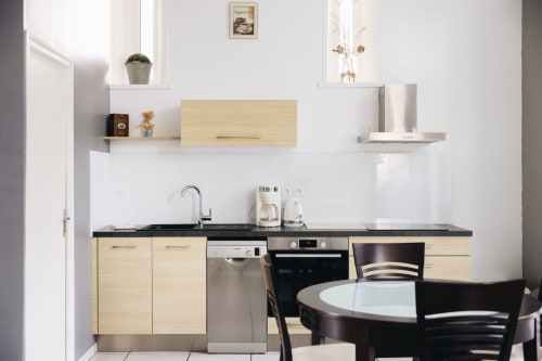 Cuisine moderne avec armoires en bois clair, plan de travail noir et salle à manger au gîte La Maison D'olivier en France