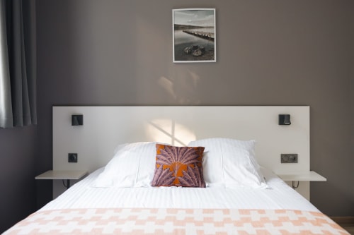 Chambre chaleureuse à La Maison D'olivier avec literie blanche, coussin orange et tableaux encadrés