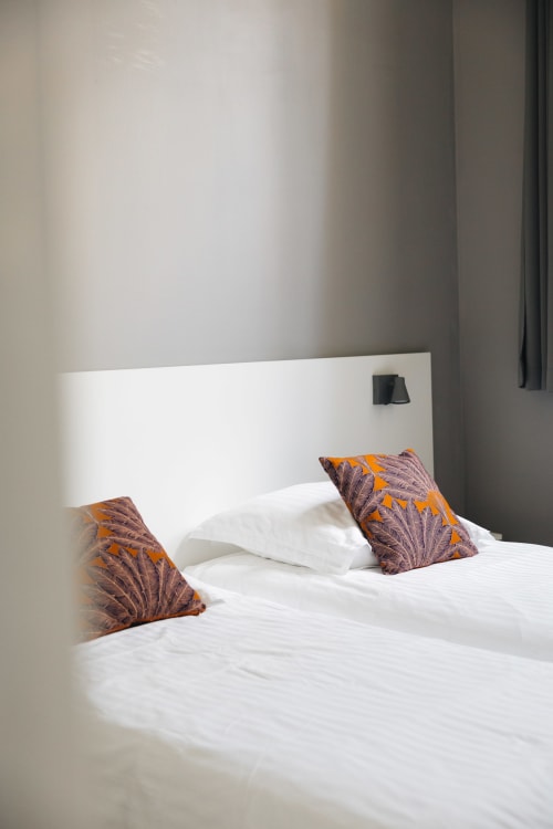 Chambre moderne du gîte La Maison D'olivier avec lit blanc, coussins décoratifs orange et violet, tête de lit épurée
