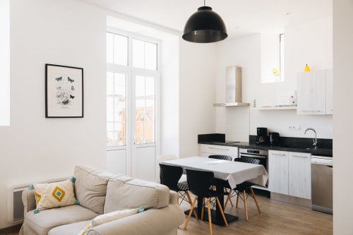 Espace de vie cottage moderne avec canapé beige, table à manger, cuisine ouverte à plan de travail noir et grandes fenêtres à La Maison