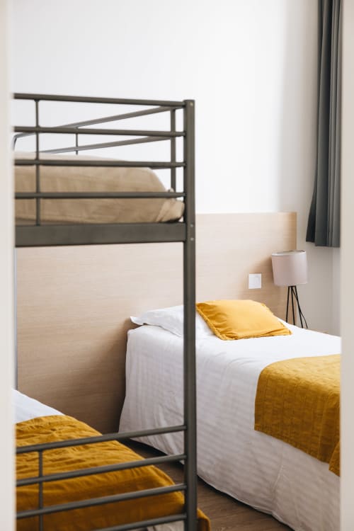 Chambre moderne du gîte La Maison D'olivier à Mesnard la Barotière avec lit en métal, literie blanche et accents jaune or
