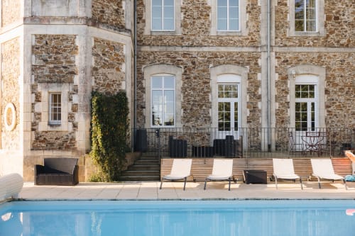 Terrasse avec piscine de La Maison D'olivier, chaises longues, façade en pierre et fenêtres cintrées