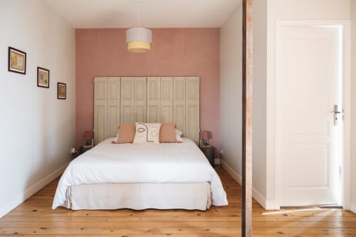 Chambre à La Maison D'olivier avec lit blanc, mur d'accent en terre cuite, tête de lit en bois et luminaire suspendu.