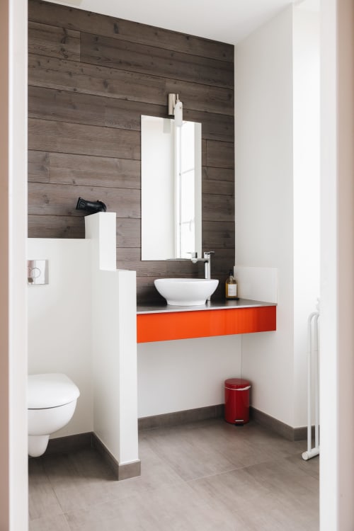 Salle de bain moderne à La Maison D'olivier B&B avec vasque blanche, meuble-lavabo orange et mur d'accent en bois foncé