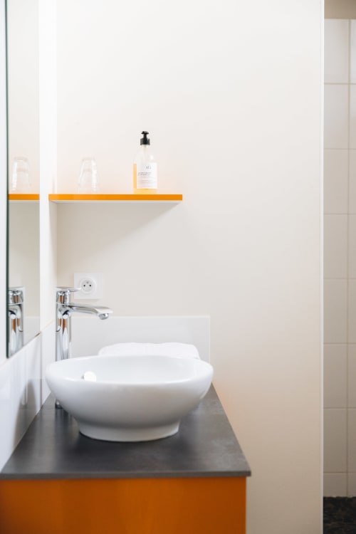 Évier moderne blanc en vasque à La Maison D'olivier B&B avec accents orange et rangement pour articles de toilette