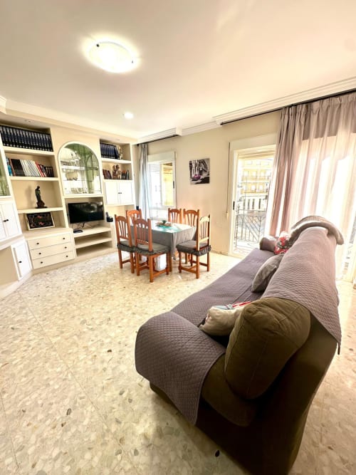 Amplio salón de apartamento en Mérida con sofá, comedor, estanterías integradas y balcón con vistas a la ciudad