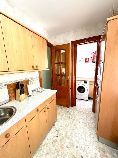 Cocina moderna con gabinetes de madera, encimeras blancas y área de lavandería en apartamento de Mérida