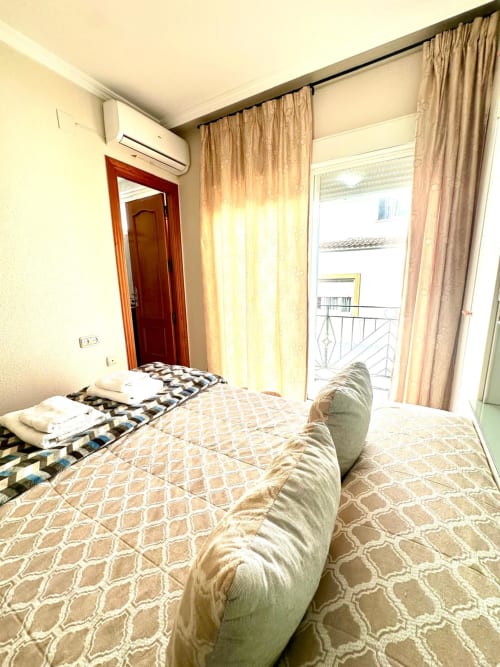 Dormitorio luminoso en Mérida con camas gemelas, balcón con vistas a la ciudad, cortinas beige y puerta de madera
