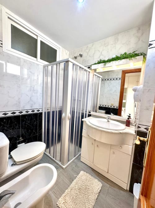 Baño moderno en apartamento de Mérida con azulejos de mármol, cabina de ducha, lavabo blanco y toallero calefactor