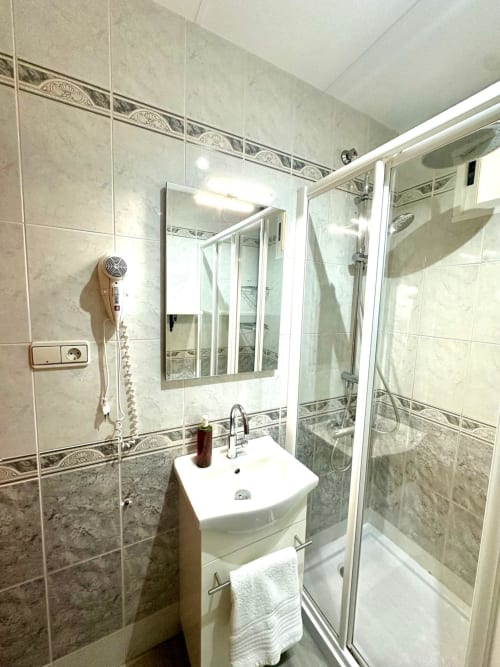 Baño moderno en apartamento de Mérida con lavamanos de pedestal blanco, espejo y cabina de ducha de cristal