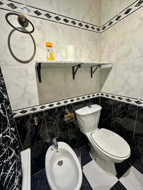 Baño moderno en apartamento de Mérida con azulejos de mármol negro, accesorios blancos y paredes superiores de mármol con cenefa decorativa