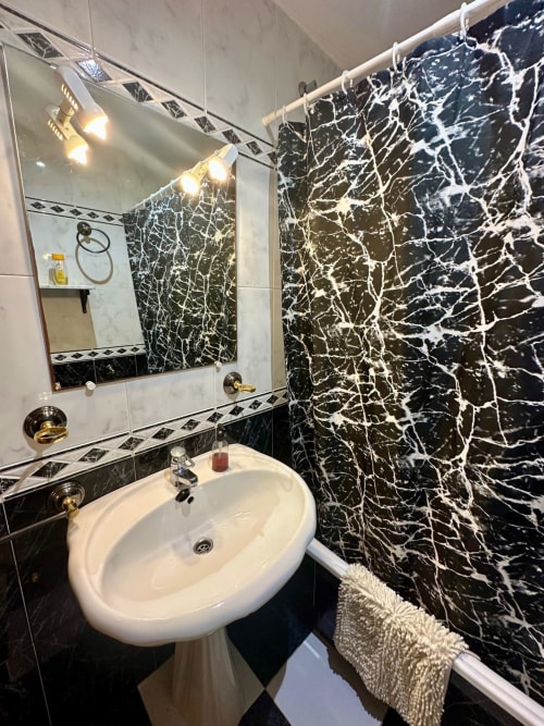 Baño moderno con paredes de mármol negro, lavabo redondo blanco y accesorios de latón en el apartamento Gestyp-AT de Mérida