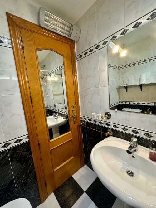Elegante baño en apartamento de Mérida con azulejos de mármol, puerta de madera, lavamanos de pedestal y cenefa decorativa en blanco y negro