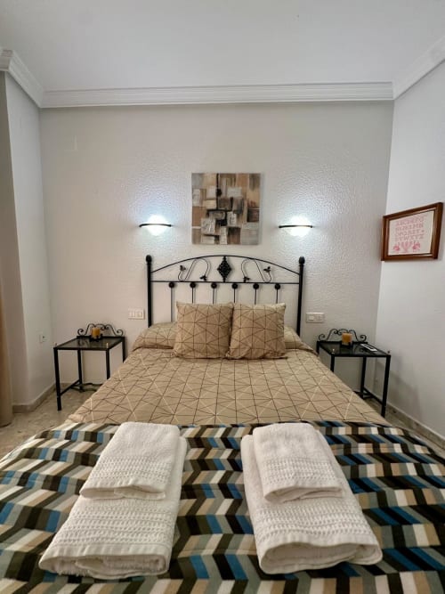 Habitación moderna en apartamento Gestyp-AT, Mérida con cama de metal negro, ropa de cama beige, mesitas gemelas y pared contemporánea