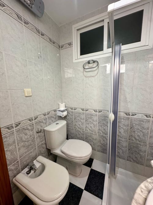 Baño moderno con doble lavabo, inodoro y ducha en el apartamento Gestyp-AT de Mérida con paredes de azulejos y vistas a la ciudad.