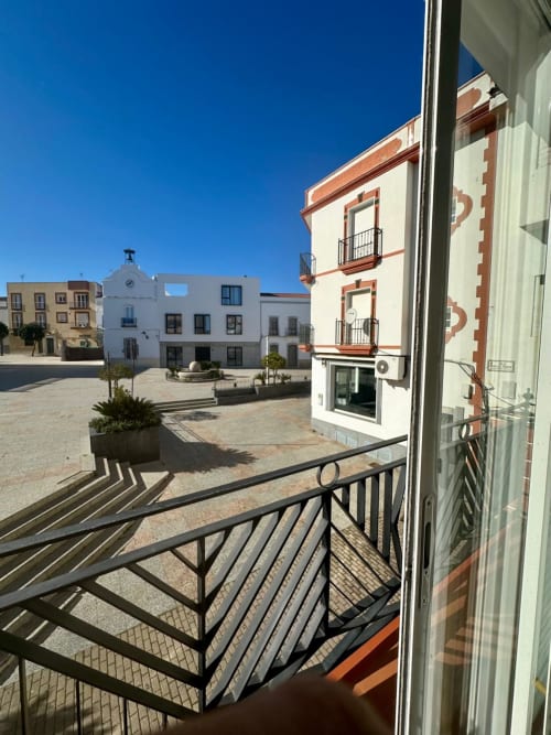 Balcón de apartamento en Mérida con vista a plaza histórica, edificios coloniales blancos y terracota bajo cielo azul despejado