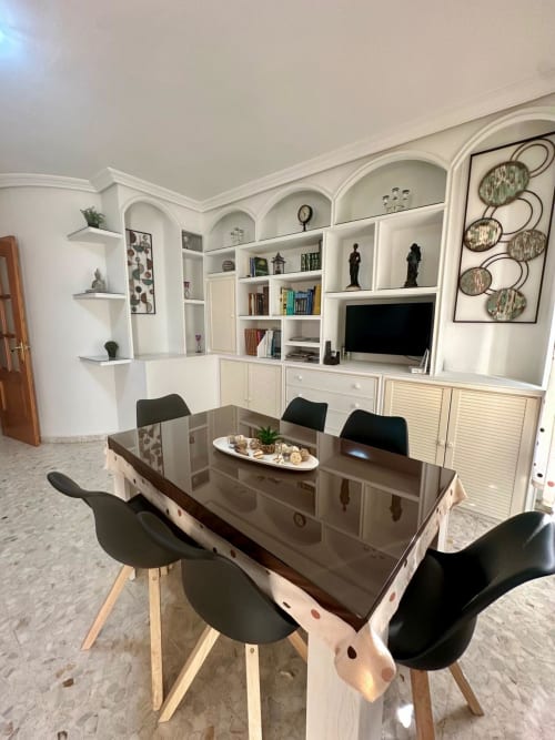 Comedor moderno en Mérida con estantería blanca, mesa de comedor oscura, sillas negras y unidad de entretenimiento con televisor