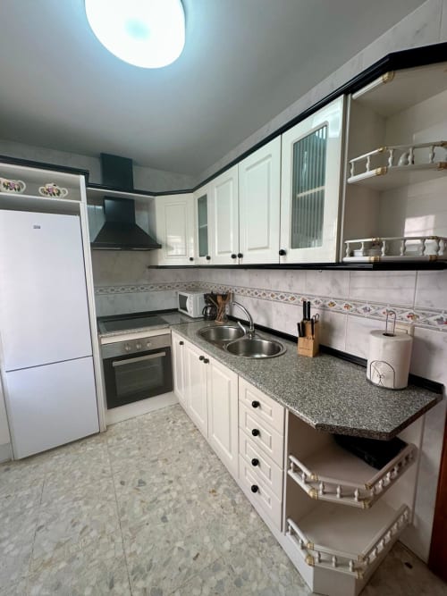 Cocina moderna en apartamento de Mérida con gabinetes blancos, encimera de granito gris, fregadero de acero inoxidable y azulejos decorativos