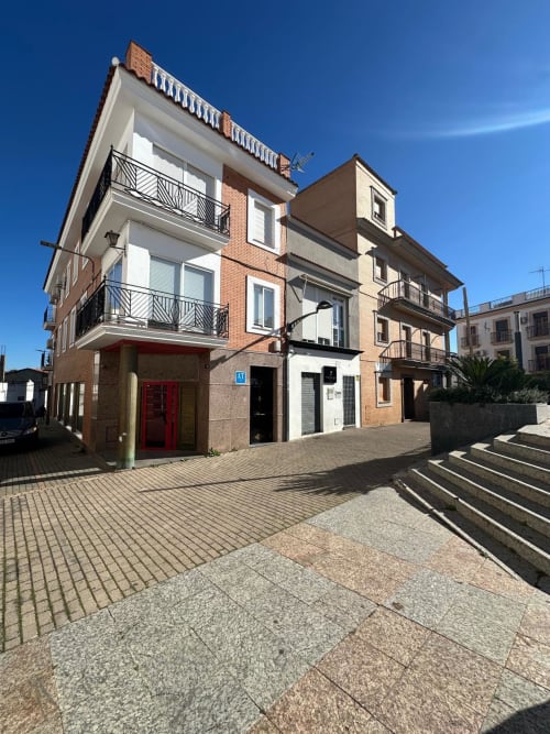 Moderno edificio de apartamentos en Mérida con entrada roja, balcones y cielo azul despejado