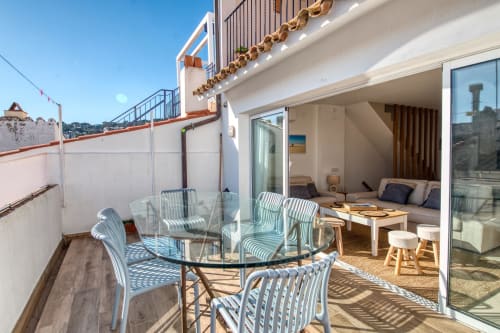 Sunny terrace at Finques Garcia Enrich in Palafrugell with dining table, striped chairs, and modern interior access