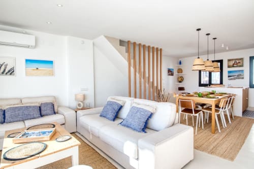Modern open-plan apartment in Palafrugell with coastal decor, beige sofas, wooden dining table, and beach-themed artwork.