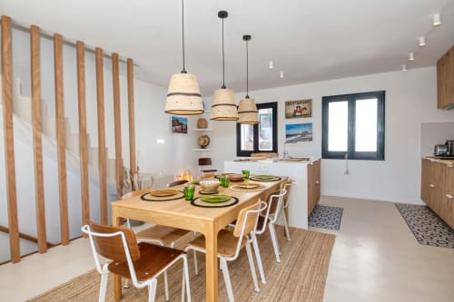 Modern dining area at Finques Garcia Enrich in Palafrugell with wooden table, pendant lights, and kitchen view