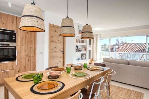 Modern dining area at Finques Garcia Enrich in Palafrugell with wooden table, woven pendant lights, and coastal views through