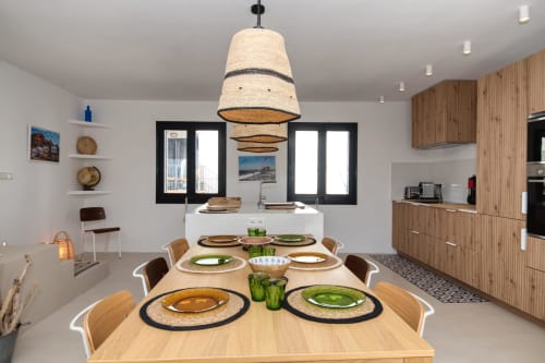 Modern dining area at Finques Garcia Enrich in Palafrugell with wooden table, woven pendant light, and contemporary kitchen