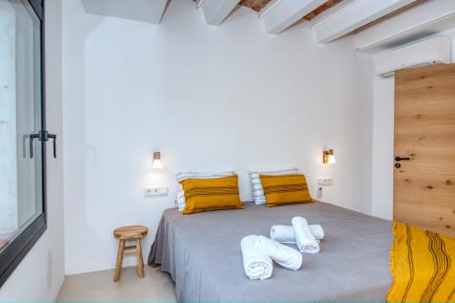 Modern bedroom at Finques Garcia Enrich with gray bed, yellow pillows, white towels, wooden door, and minimalist decor in