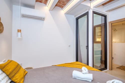 Modern bedroom at Finques Garcia Enrich in Palafrugell with exposed beams, yellow accents, and ensuite bathroom