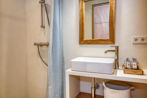 Modern bathroom at Finques Garcia Enrich, Palafrugell with white vessel sink, wooden mirror, and shower area.