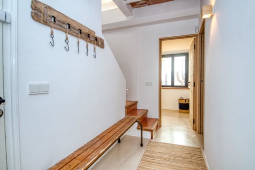 Bright entryway at Finques Garcia Enrich in Palafrugell with wooden bench, rustic hooks, and doorway to bedroom.