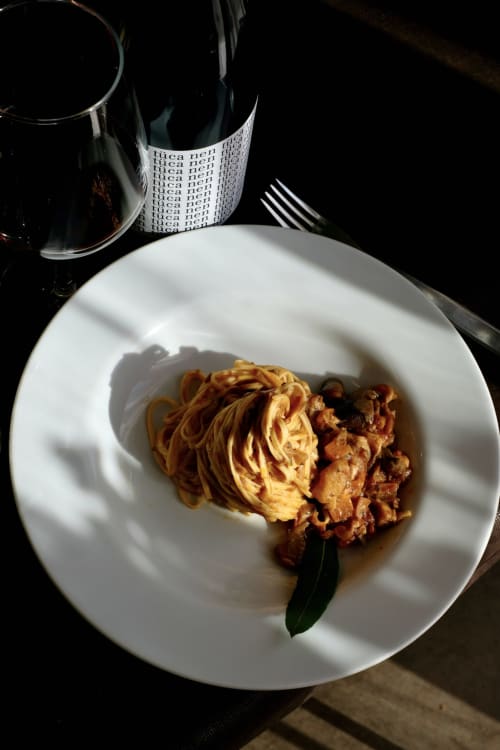 Piatto di pasta elegantemente impiattato con carni ad Agorà Calamandrana, accompagnato da bicchiere di vino e mise en place