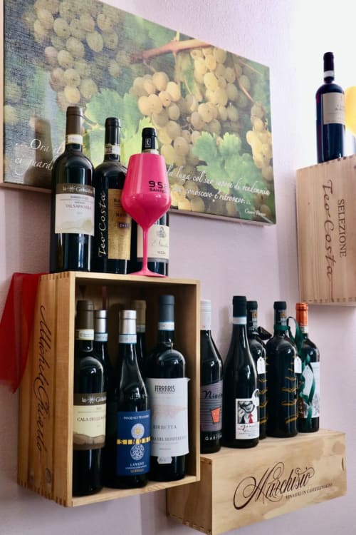 Scaffale espositivo di vini presso l'hotel Agorà Calamandrana con vini italiani e calice rosa