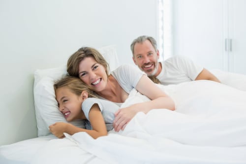 Famiglia felice che si rilassa sul letto bianco dell'hotel Agorà Calamandrana in Italia
