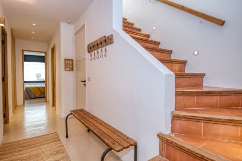 Bright hallway with wooden stairs, bench seating, and terracotta tile steps in a Palafrugell coastal cottage rental property