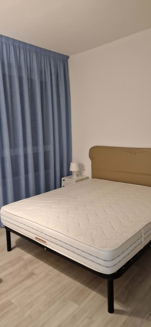 Modern bedroom at Lamar Suites Seafront with white mattress, tan headboard, blue curtains, and minimalist decor