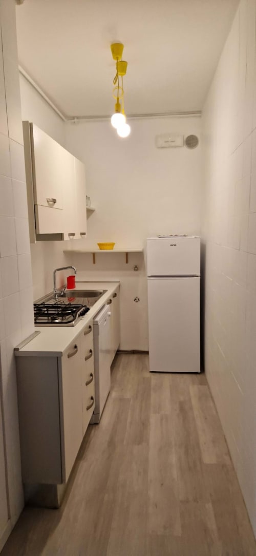 Compact modern kitchen in Lamar Suites Seafront Apartments with gas stove, refrigerator, and yellow pendant light fixture