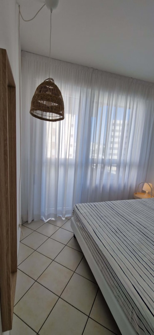 Modern bedroom with woven pendant light, striped bed, tile flooring, sheer curtains, and sea view at Lamar Suites Seafront