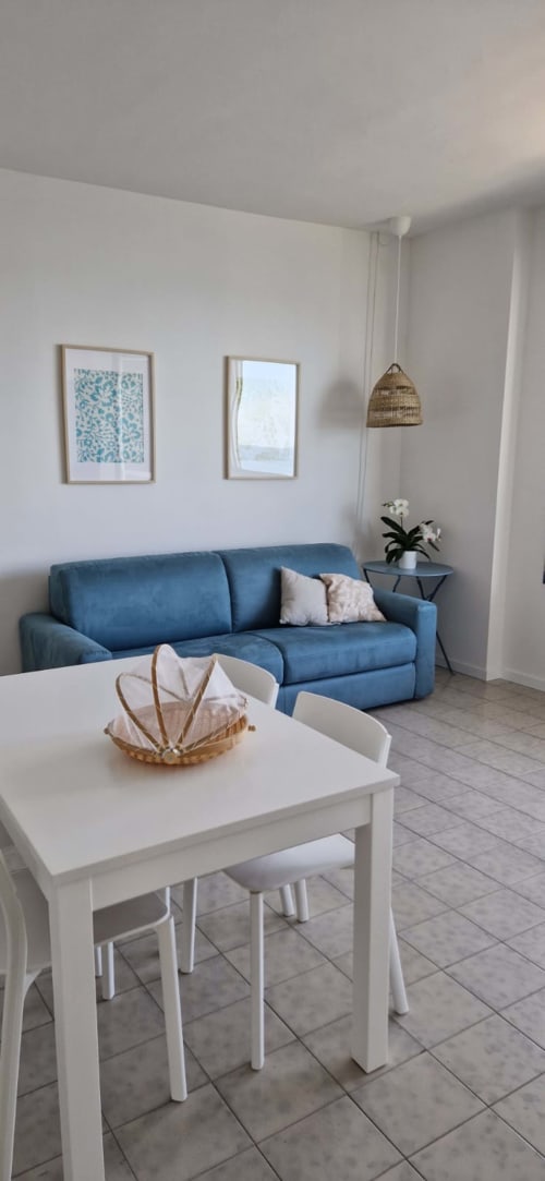 Modern living room at Lamar Suites with blue sofa, white dining table, framed artwork, and sea view from balcony in Misano