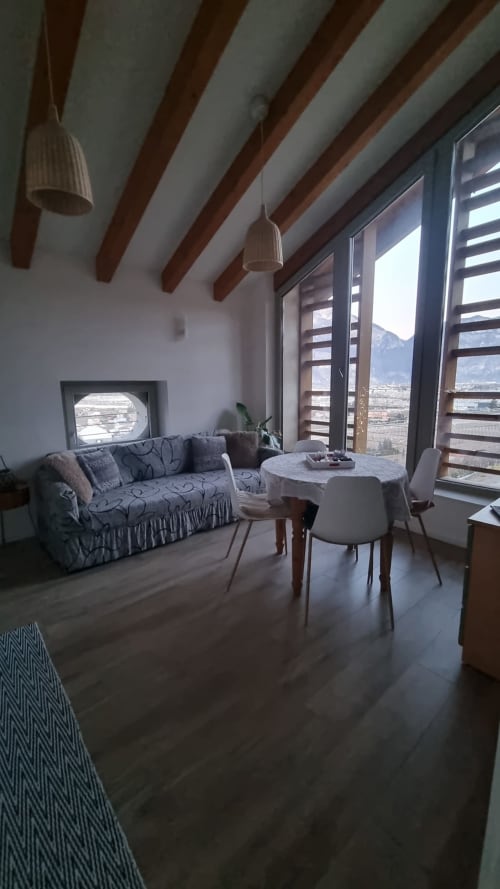 Appartamento con vista montagna a Maso Kreuzberg a Trento con travi a vista, divano, tavolo da pranzo e finestre panoramiche