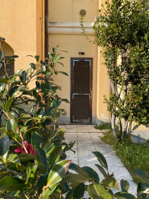 Ingresso della corte giardino dell'Apartment Roma 1 in THE V Collection a Turate, con lussureggiante vegetazione e porta scura