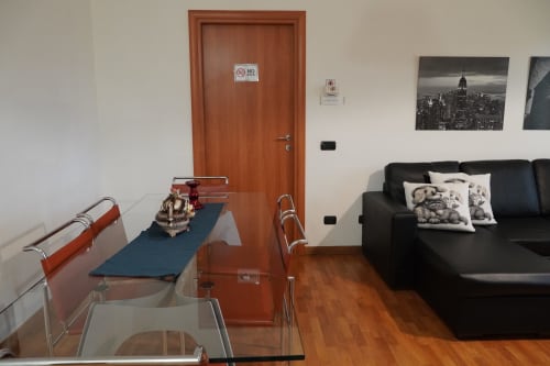 Appartamento Roma 1 con soggiorno con divano nero, scrivania, porta in legno e opere d'arte con skyline cittadino presso THE V Collection a Turate