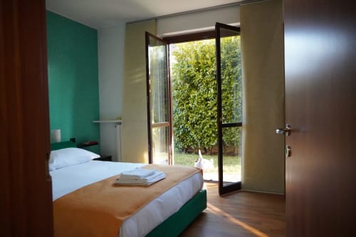 Camera moderna in THE V Collection Roma 1 Apartment con parete accento verde, biancheria bianca e vista giardino attraverso vetrate