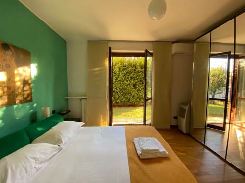 Camera da letto moderna con parete accent verde, letto bianco, guardaroba a specchio e porte vista giardino - Roma 1 Apartment, THE V