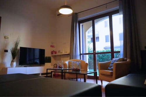 Soggiorno moderno dell'Appartamento Roma 2 presso THE V Collection, Turate, con TV, poltrone beige, tavolo in vetro e vista sul giardino